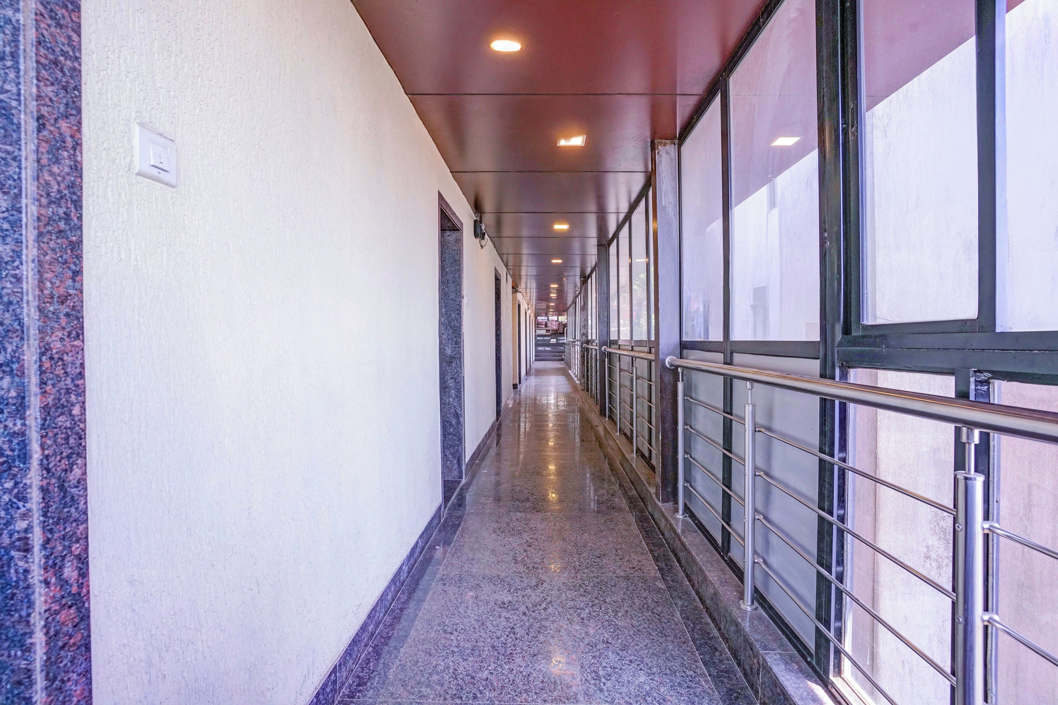 A long, narrow corridor with a polished floor, metal railings, and large windows on one side.