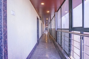 Un pasillo largo y estrecho con piso pulido, barandillas metálicas y grandes ventanales en un lado.