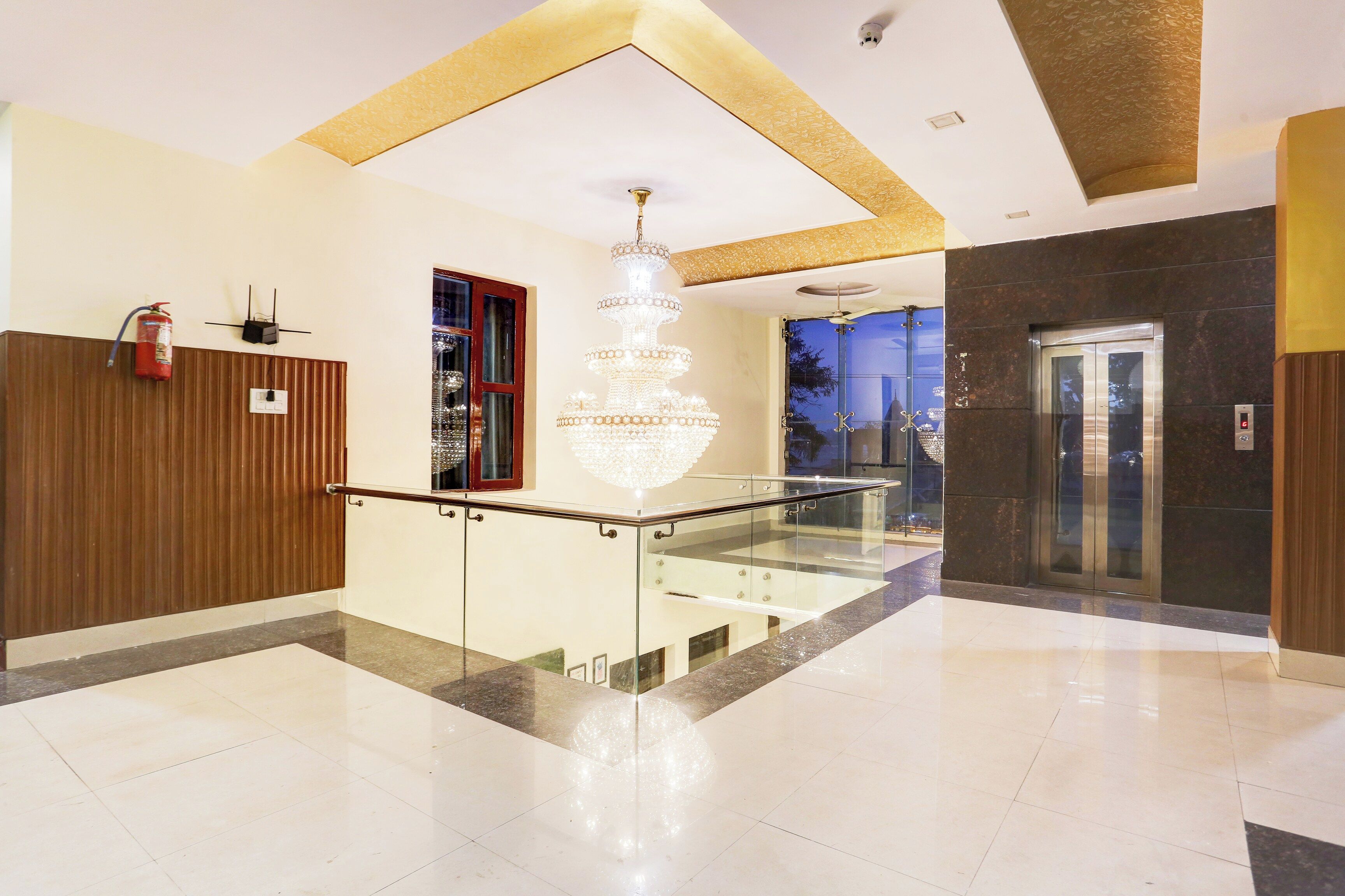 A modern lobby with a glass railing, a chandelier, and an elevator.