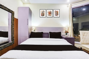 Habitación de hotel con una cama grande, un armario, un espejo, una mesita de noche con un florero y obras de arte enmarcadas en la pared.