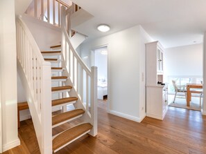 Eine Treppe mit Holzboden und weißen Geländern führt zu einem Schlafzimmer mit einem Bett und einem Nachttisch.