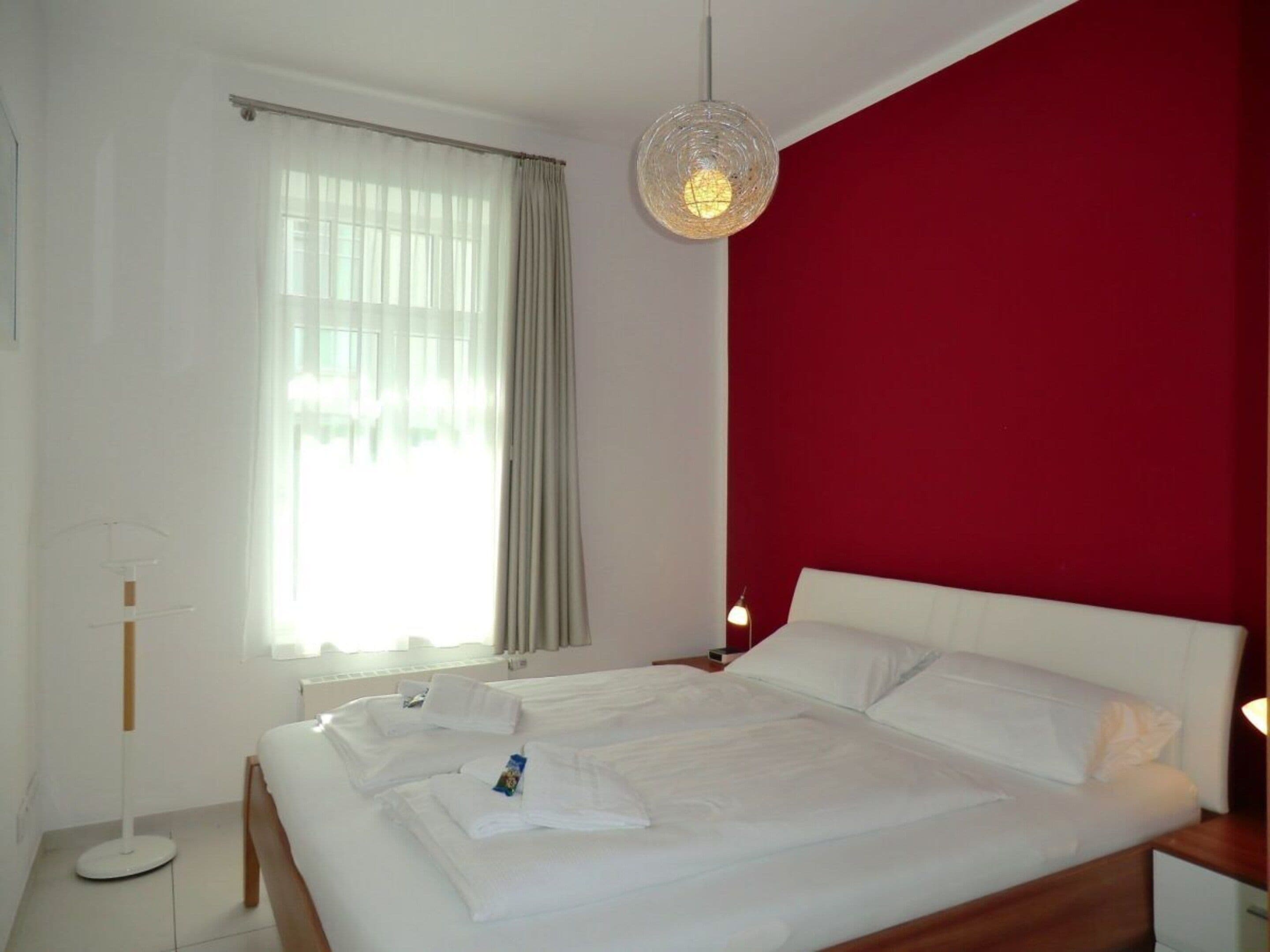 Une chambre d’hôtel avec un lit, une table de chevet, une lampe de chevet, un lampadaire et une fenêtre avec des rideaux.