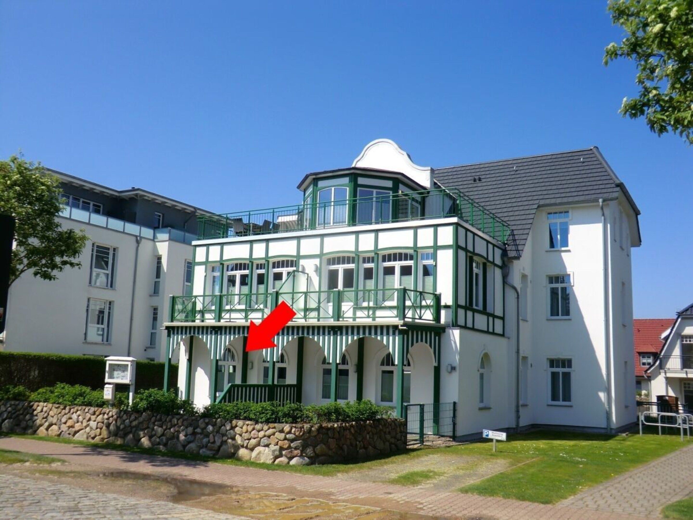 A two-story building with a white facade and green accents, featuring a balcony with a red flag.