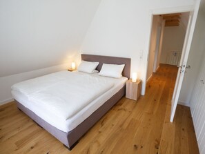 Ein Einzelbett mit Holz-Kopfstück in einem Zimmer mit Holzboden und weißen Wänden.