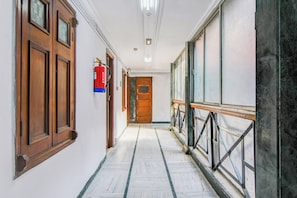 Un pasillo con puertas de madera, un extintor y suelo de mármol.