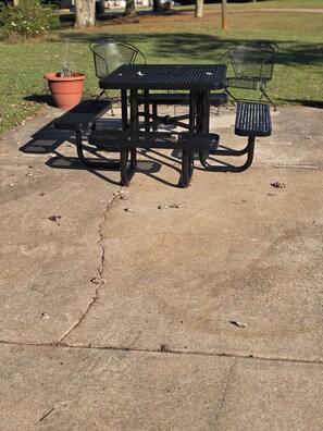 A concrete patio with a metal table and chairs, a potted plant, and a crack in the pavement. - Wonderful 2-bedroom house with AC in Winterville (Winterville)