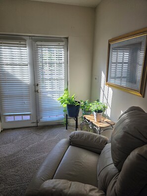 A living room with a beige sofa, a small table with a potted plant, and a door with blinds. - Wonderful 2-bedroom house with AC in Winterville (Winterville)