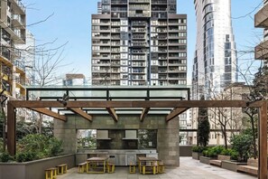 Un espacio al aire libre con patio, una pérgola, asientos y vistas a edificios altos.