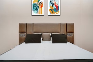 Una habitación de hotel con una cama grande, dos mesitas de noche, un cabecero y dos cuadros abstractos en la pared.