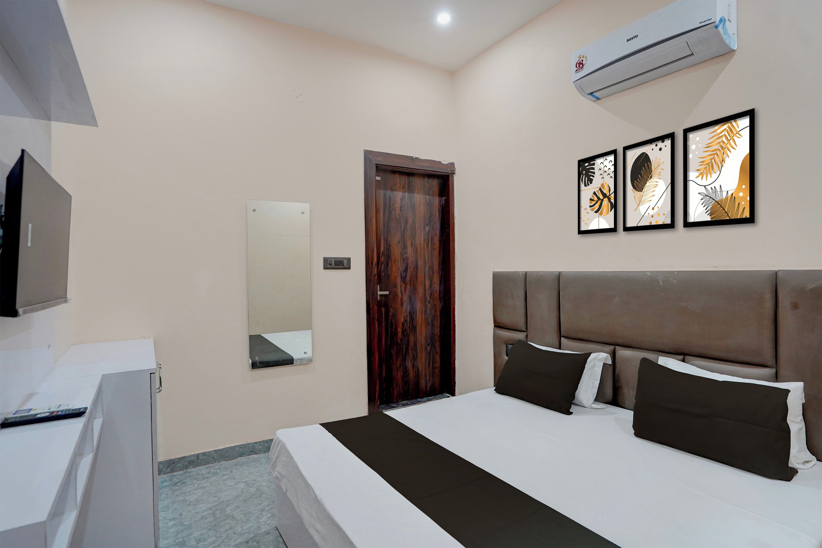 Una habitación de hotel con cama, escritorio, aire acondicionado, espejo y cuadros en la pared.