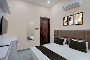 Una habitación de hotel con cama, escritorio, aire acondicionado, espejo y cuadros en la pared.