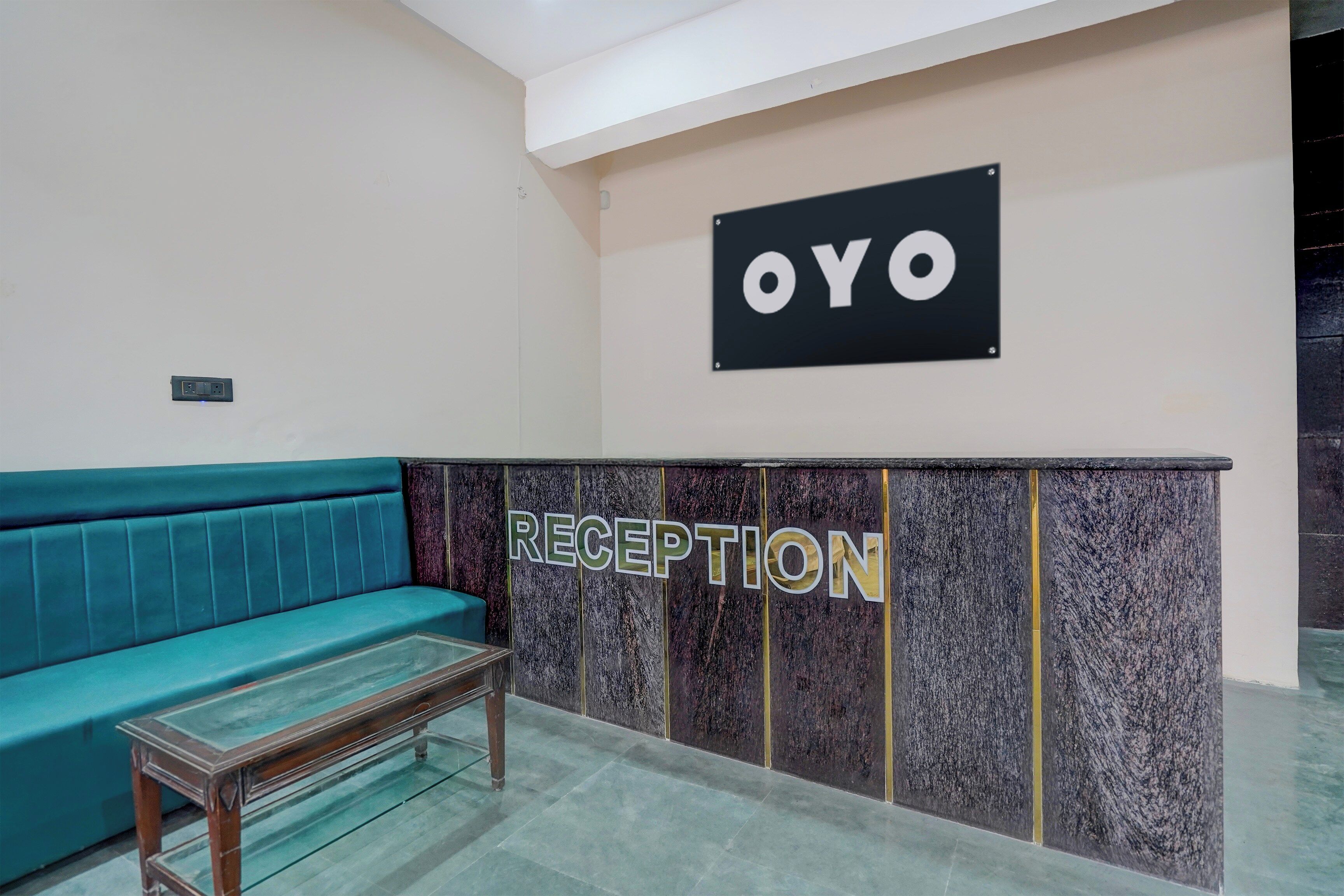 Et receptionsområde med en turkis sofa, en receptionsdisk og et skilt med teksten 'OYO RECEPTION'.