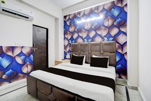 A hotel room with a bed, a headboard, a wall with a leaf pattern, an air conditioning unit, and a door. - Hotel O R K HOTEL (Agra)