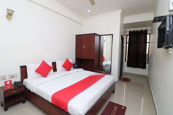 Habitación de hotel con cama, armario, mesita de noche con teléfono, televisor montado en la pared y felpudo rojo.