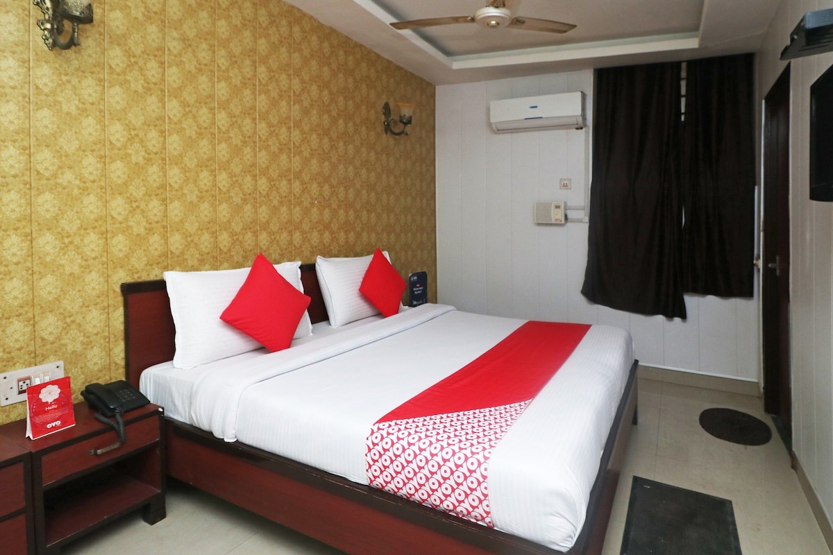 A hotel room with a bed, a bedside table with a phone, and an air conditioning unit on the wall.