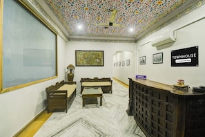 Un área de recepción con mostrador, una zona de estar con sofá y sillones, un ventanal grande y un techo decorativo.