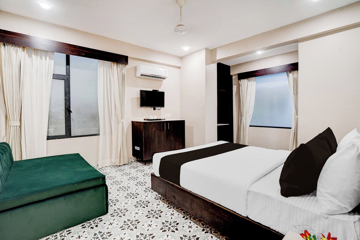 Habitación de hotel con una cama, un sofá verde, un televisor y un equipo de aire acondicionado.