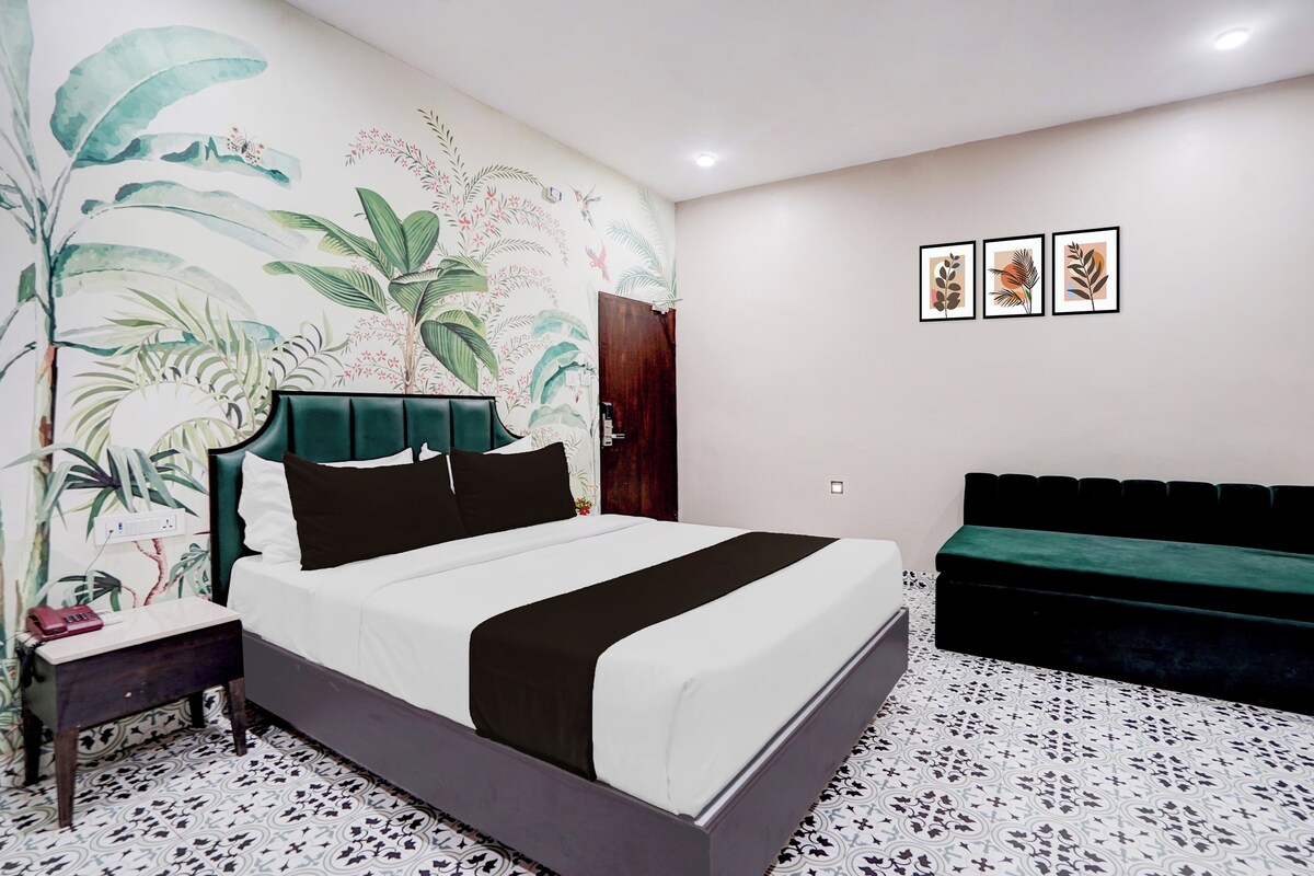 Un dormitorio con una cama, una mesita de noche, un aparador, un sofá verde y una pared con obras de arte enmarcadas.