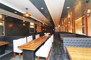 A restaurant interior with long wooden tables, white upholstered booths, and pendant lighting. - HOTEL O 03 TOWN HOUSE Shaheed Captain (Agra)