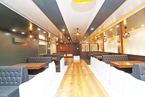 Un interior de restaurante con una mesa de madera larga, cabinas acolchadas e iluminación colgante.