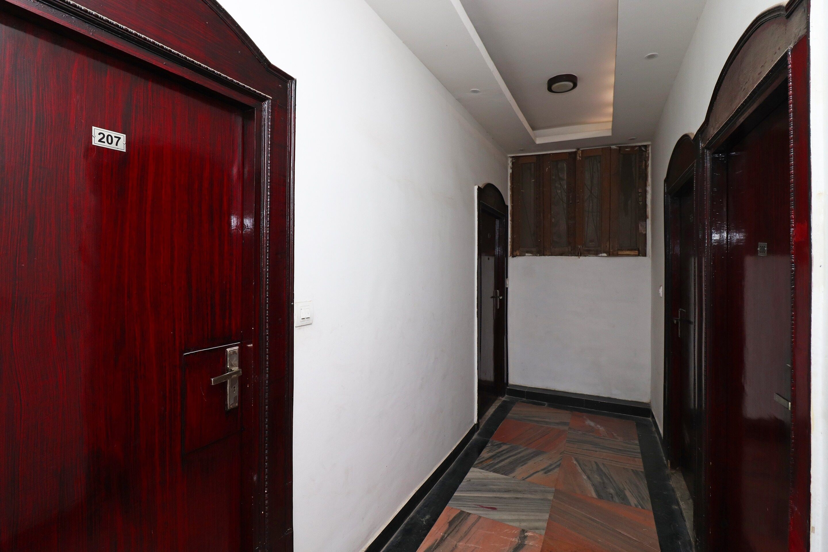 Un pasillo con una puerta roja marcada '207', una pared blanca y un piso con diseño.