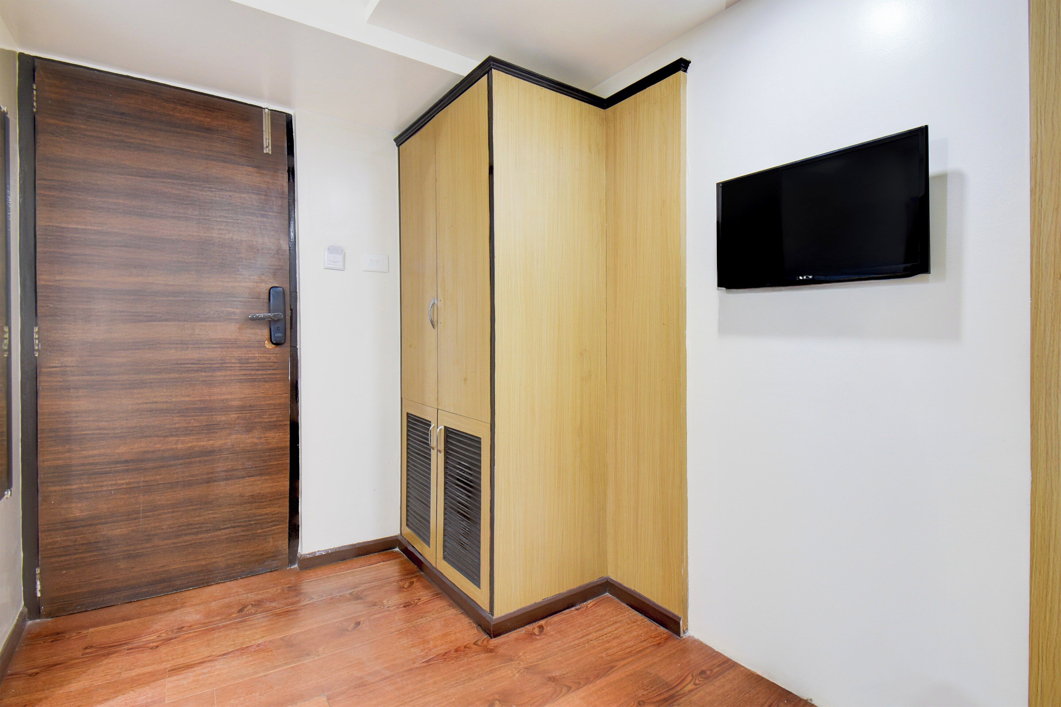 Una habitación con puerta de madera, un armario, un televisor montado en la pared y piso de madera.