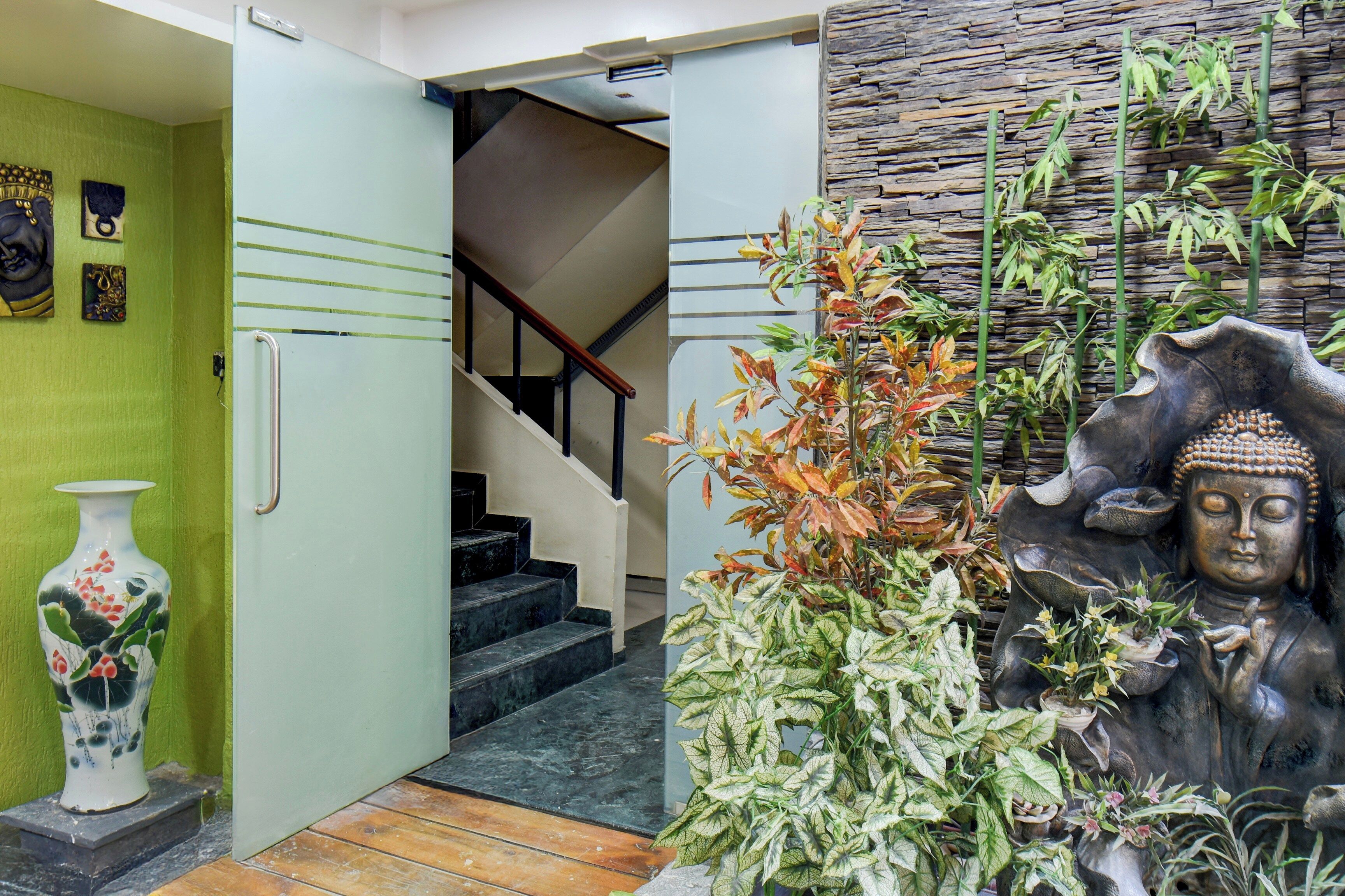 Una escalera que lleva a un segundo piso, una pared verde con obras de arte y una estatua de Buda con plantas.