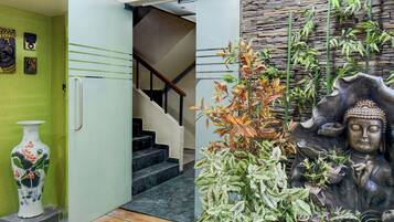Una escalera que lleva a un segundo piso, una pared verde con obras de arte y una estatua de Buda con plantas.
