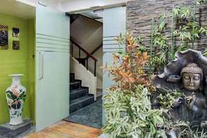 A staircase leading to a second floor, a green wall with artwork, and a Buddha statue with plants. - Townhouse Viman Nagar Business Stay (Pune)