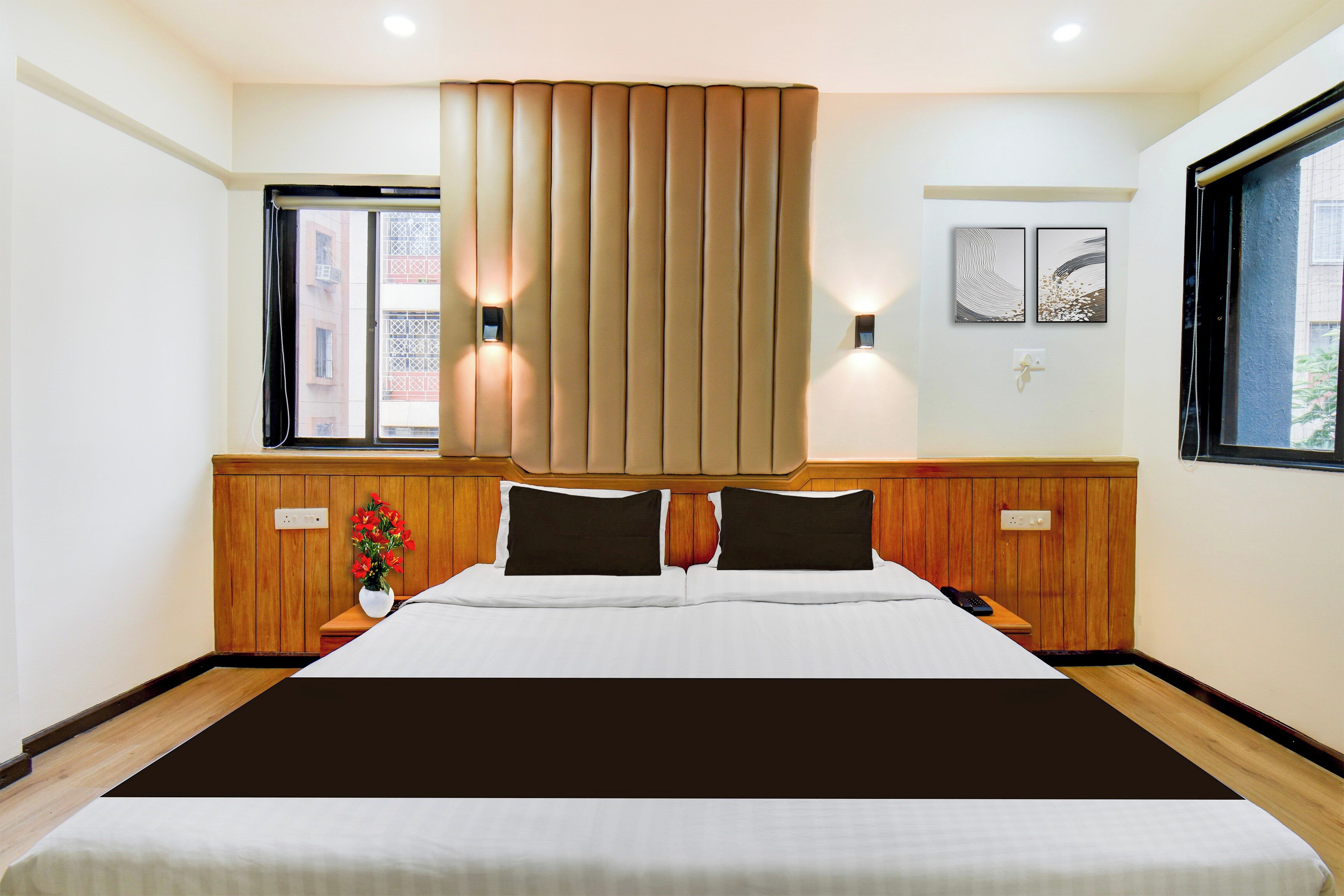 Habitación de hotel con una cama grande, cabecera de madera, dos mesitas de noche, una ventana con persianas e iluminación en la pared.