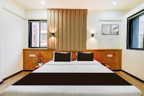 Habitación de hotel con una cama grande, cabecera de madera, dos mesitas de noche, una ventana con persianas e iluminación en la pared.