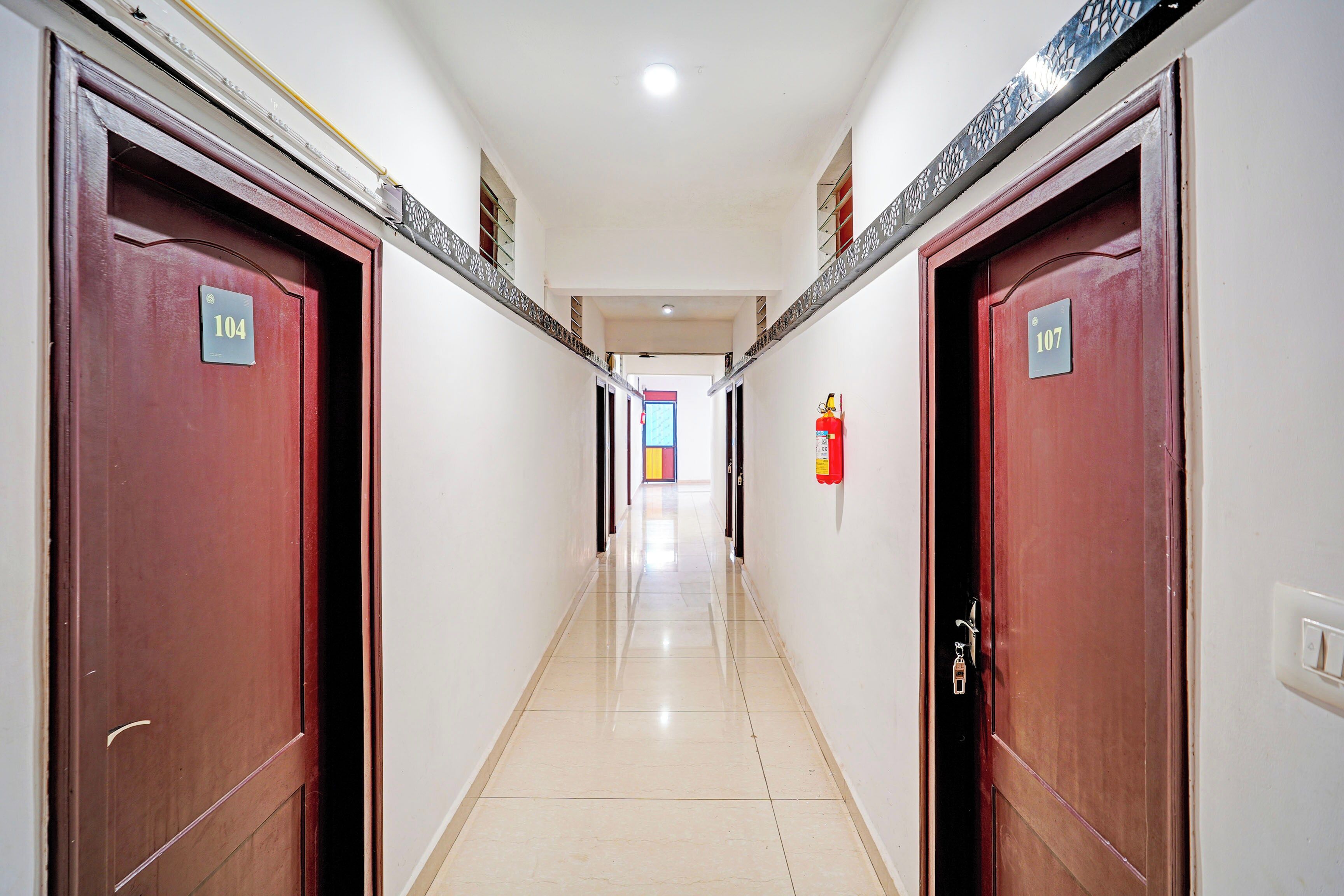 Un pasillo con puertas numeradas 104 y 107, un extintor en la pared y suelo de baldosas.