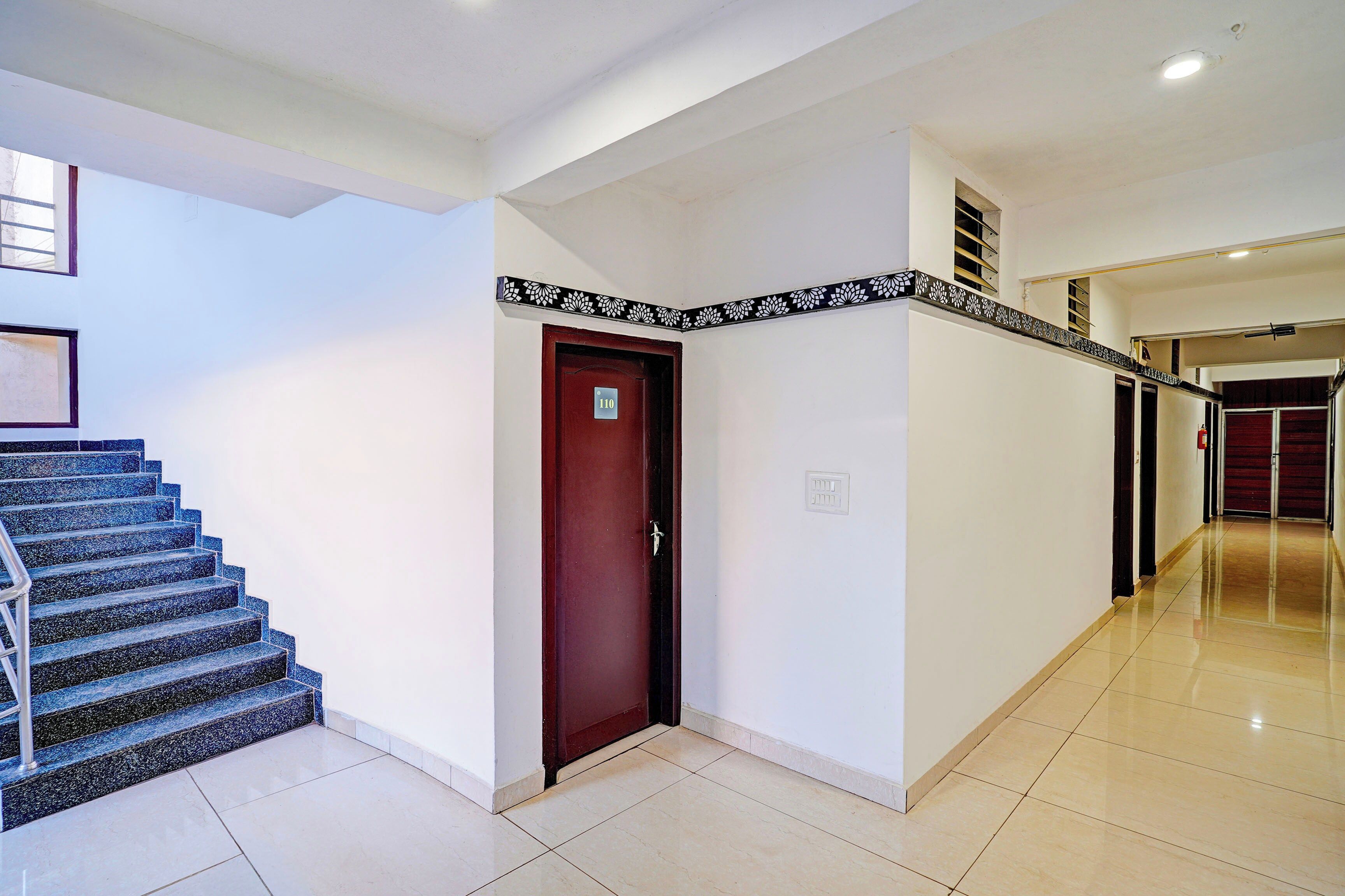 Un pasillo de hotel con una escalera, una puerta con un número y un borde decorativo en la pared.
