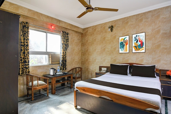 Una habitación de hotel con cama, escritorio, silla, ventilador de techo y cuadros en la pared.