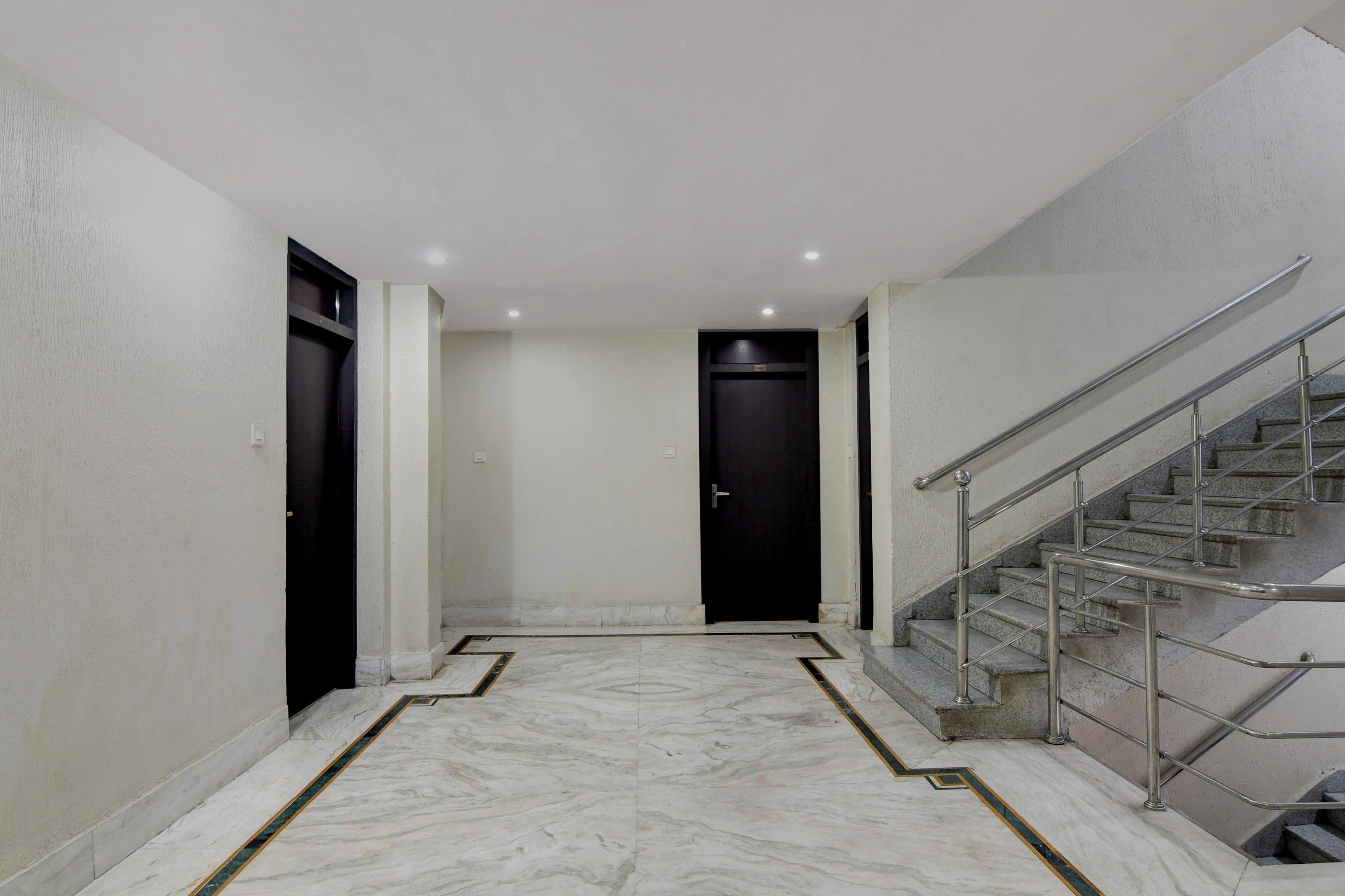 A hallway with a marble floor, a black door at the end, and a staircase with metal railings.