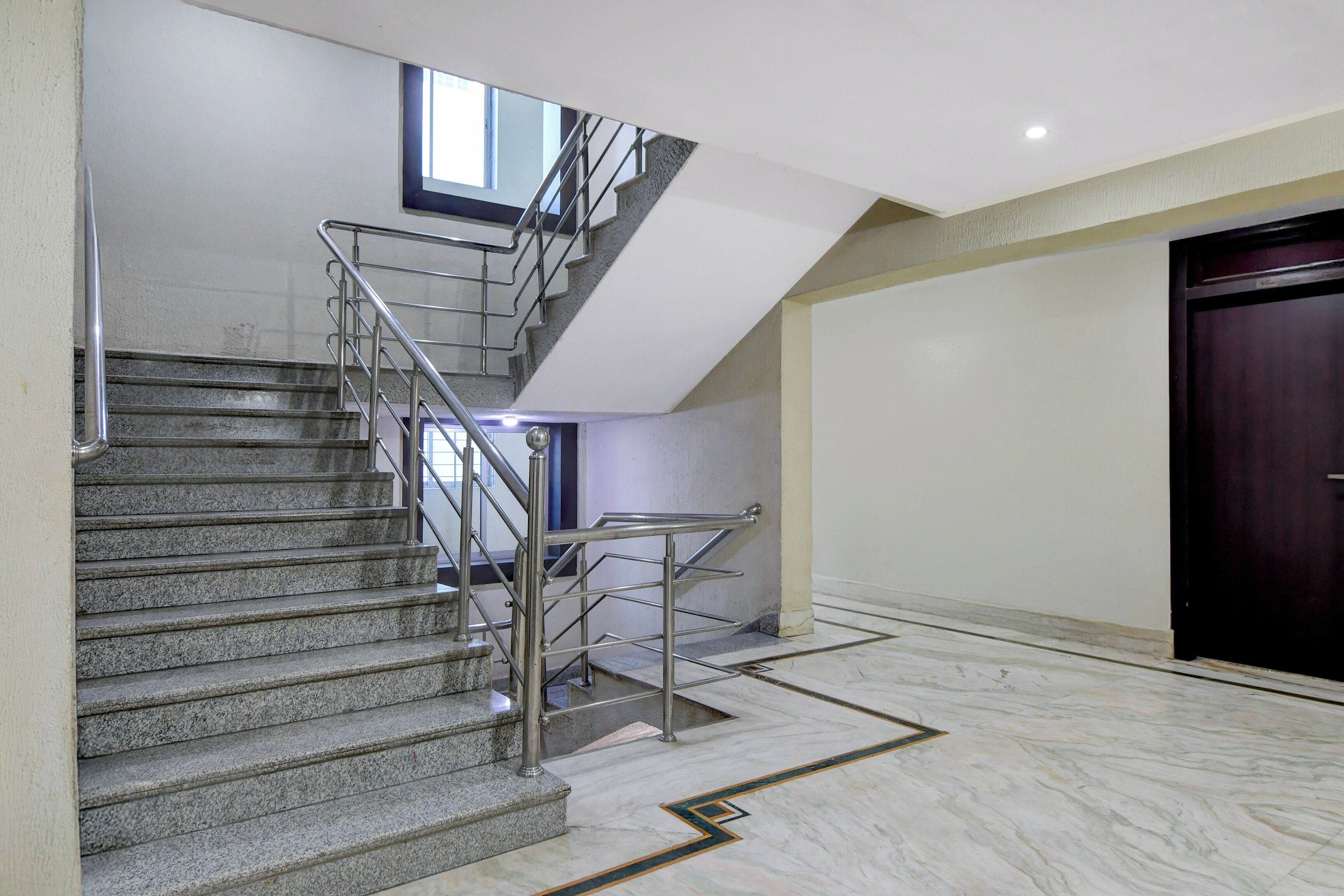 Un interior moderno con una escalera de granito, barandas de metal y un suelo de mármol.