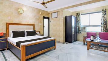A hotel room with a bed, a desk, a chair, a wardrobe, a ceiling fan, and a window with curtains.
