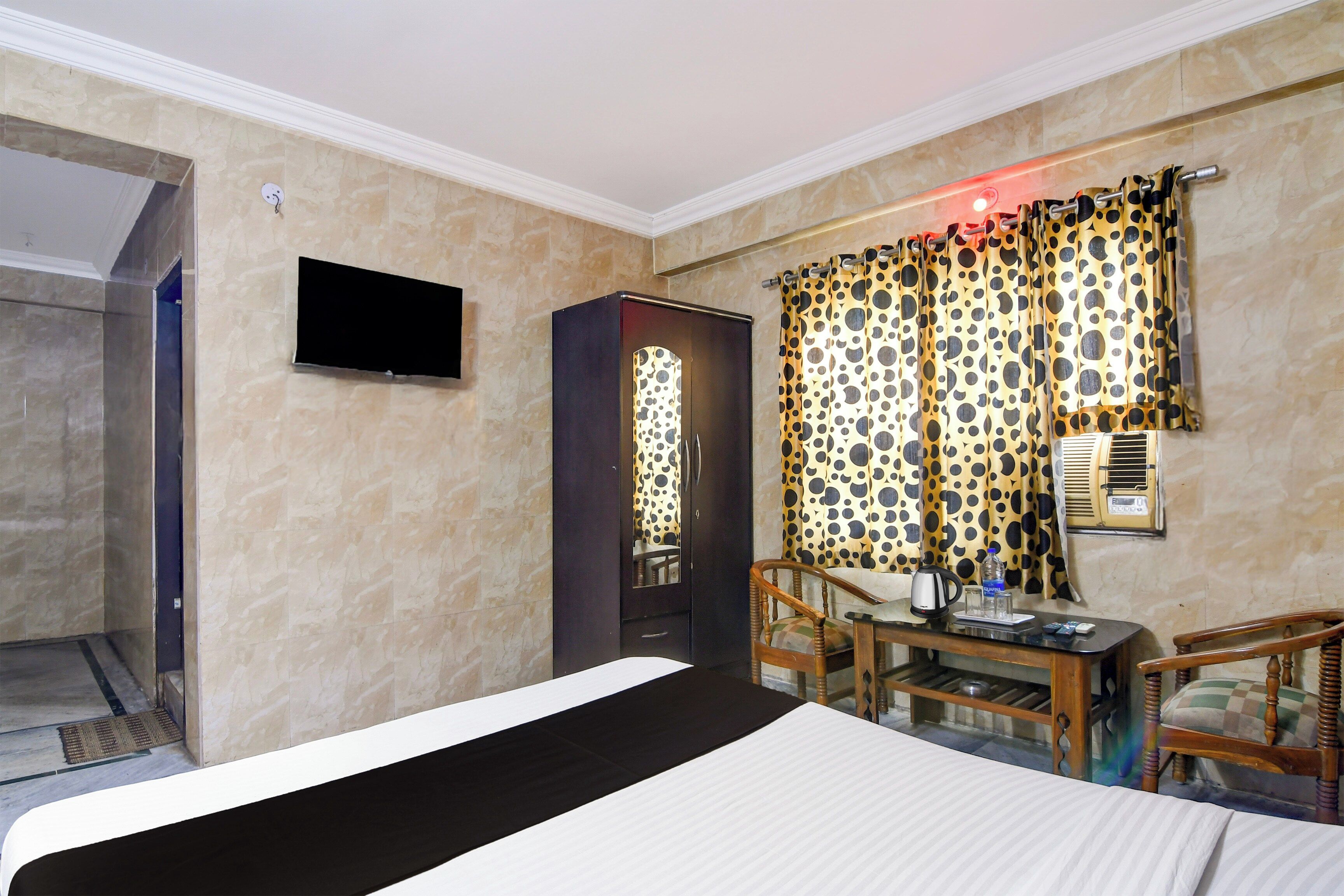 A hotel room with a bed, a desk with a chair, a television, and a window with curtains.