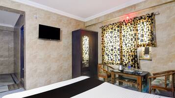 A hotel room with a bed, a desk with a chair, a television, and a window with curtains.