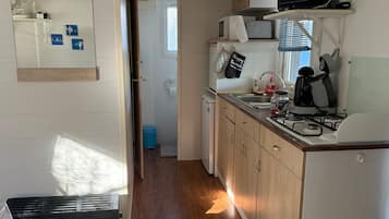 Een compacte keuken met een magnetron, fornuis en gootsteen. Ook zichtbaar is een kleine prullenbak en een deur die naar een andere kamer leidt.