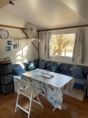 A cozy room with a sofa, a table with a tablecloth, a fan, a clock, and a window with curtains. - Mobile Home 'L Escale Cocooning D'hourtin' with Shared Pool and Private Terrace (Hourtin)
