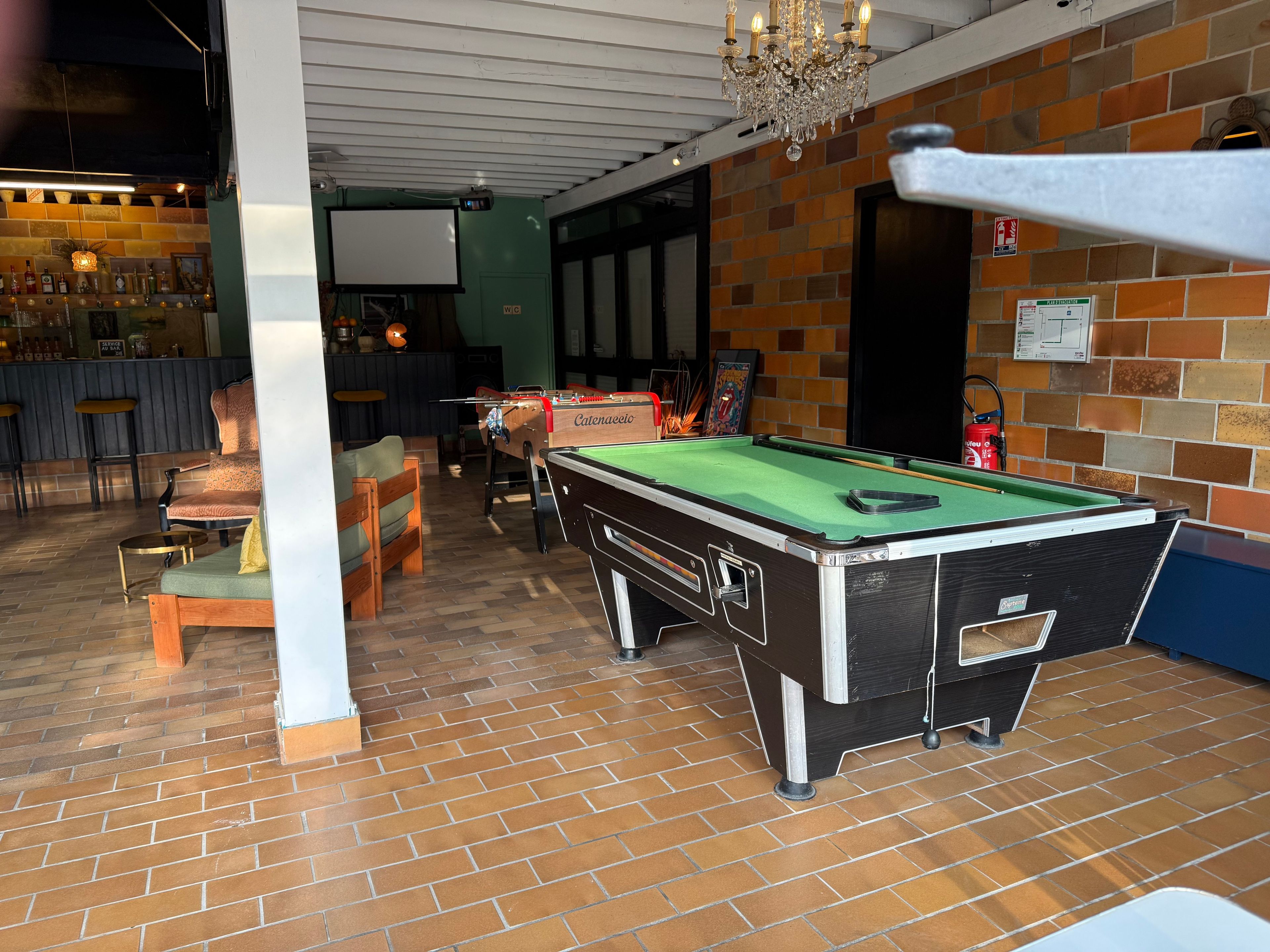 Una mesa de billar en una sala con suelo de ladrillo, una zona de bar con taburetes y un candelabro.