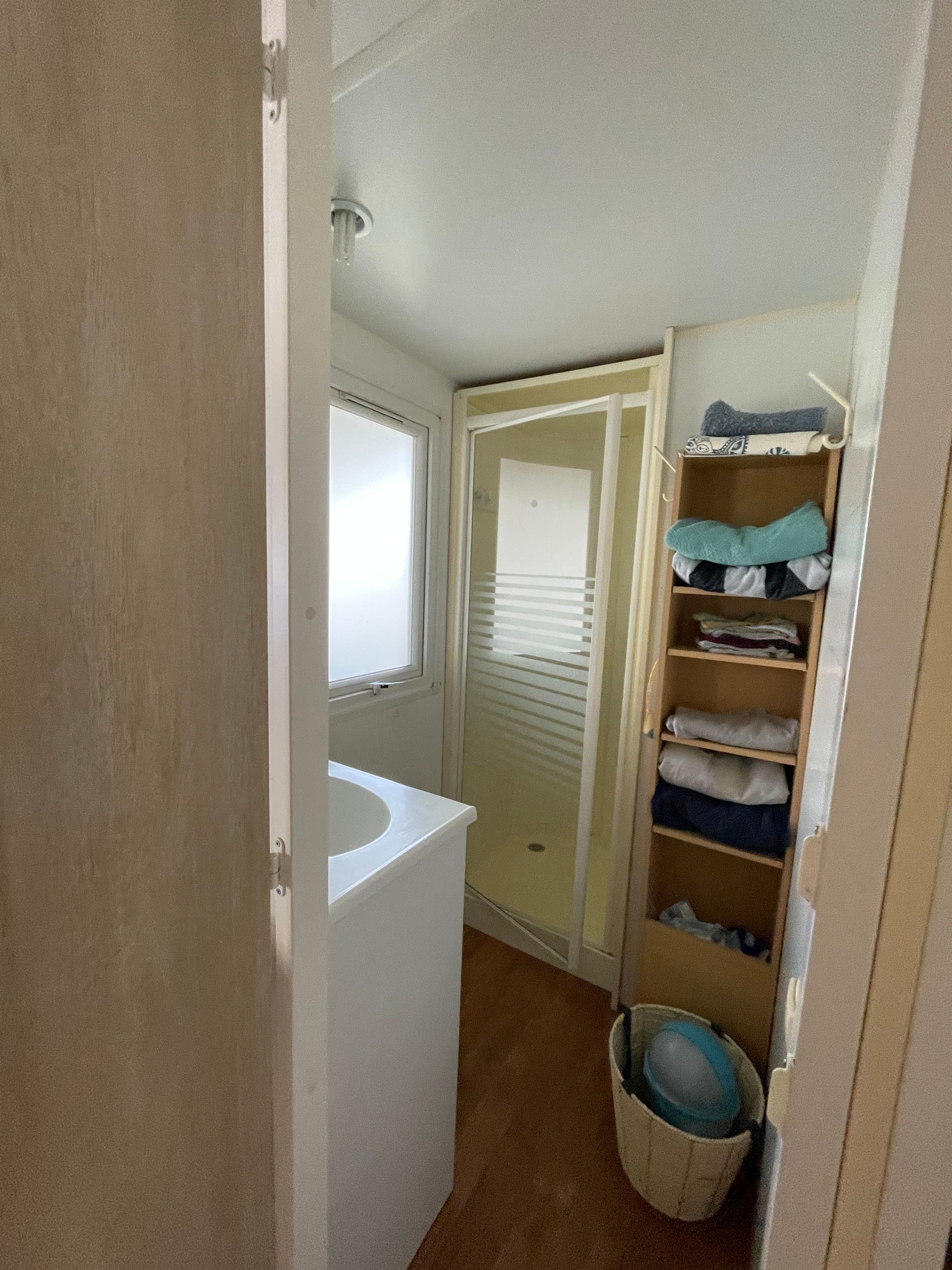 Un baño pequeño con un lavamanos blanco, cabina de ducha y un armario con estantes.