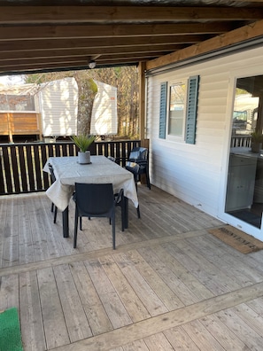 A covered outdoor patio with a table and chairs, a wooden deck, and a white building with green shutters. - Mobile Home 'L Escale Cocooning D'hourtin' with Shared Pool and Private Terrace (Hourtin)