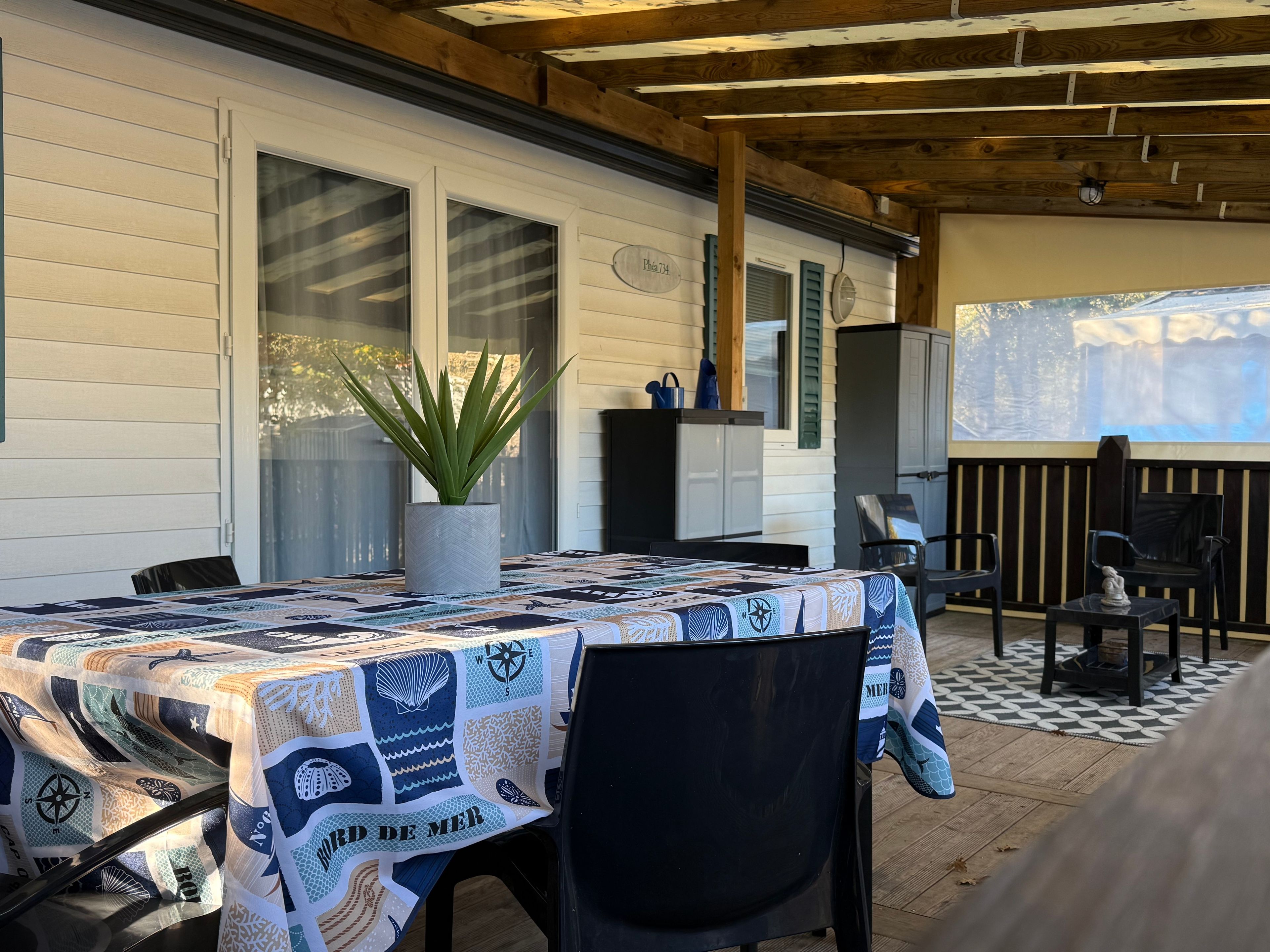 Une terrasse extérieure avec une table recouverte d’une nappe à motifs, une plante en pot et une plateforme en bois.