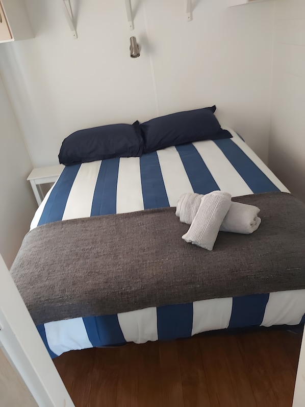A bed with a striped blue and white bedding, a dark blue pillow, and a rolled white towel. - Mobile Home 'L Escale Cocooning D'hourtin' with Shared Pool and Private Terrace (Hourtin)