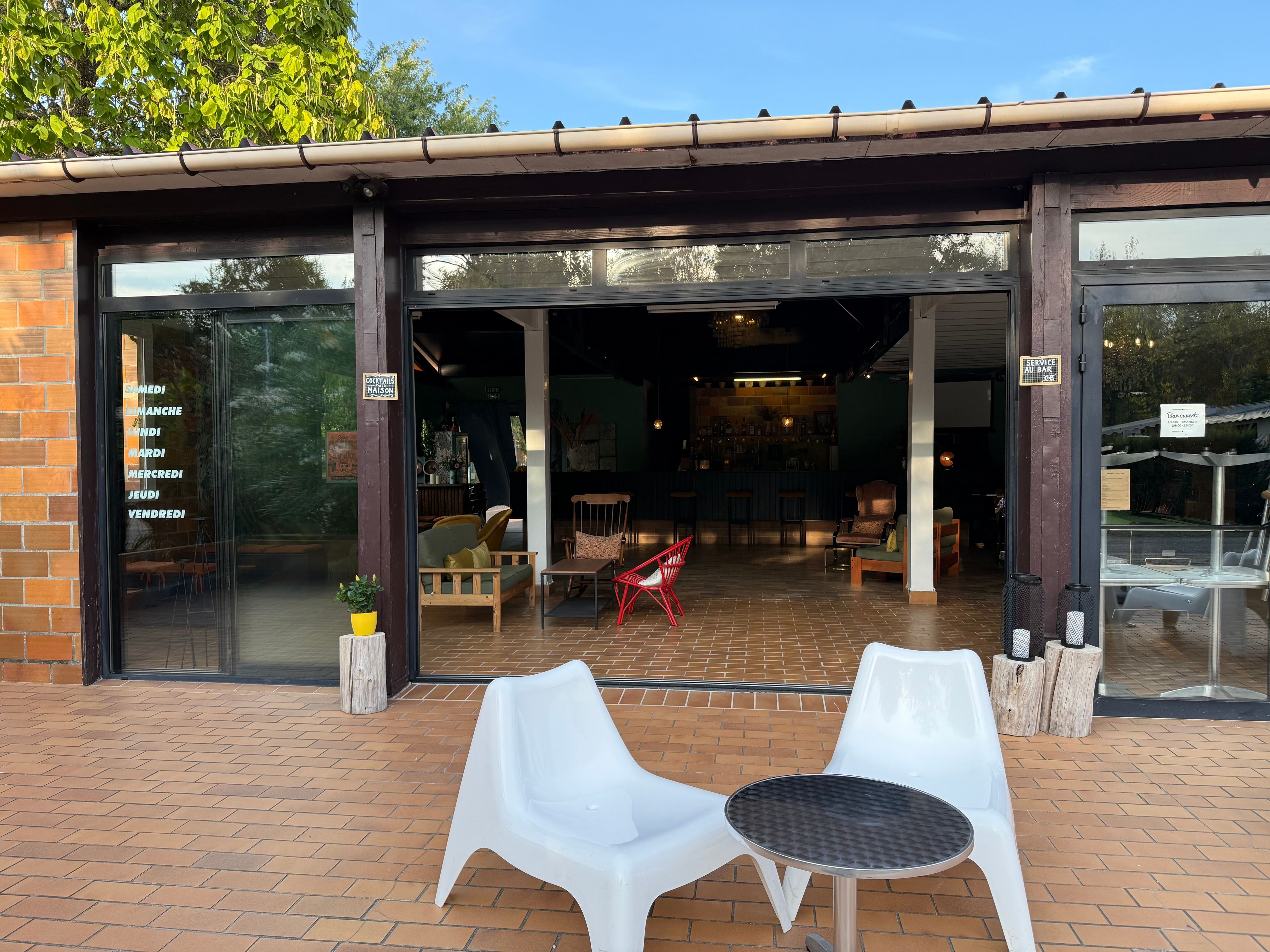 Café con mesas al aire libre, fachada de ladrillo y un letrero que indica el horario de atención.