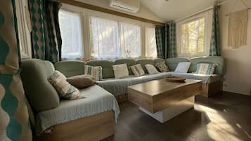 Un salon chaleureux avec un canapé d’angle, une table basse en bois et de grandes fenêtres ornées de rideaux.
