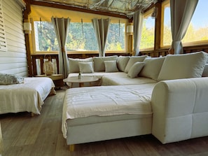 A cozy room with a bed, a sofa, and a small table, featuring wooden flooring and large windows. - Mobile Home 'Tout Confort' with Shared Pool, Wi-Fi and Air Conditioning (Hourtin)