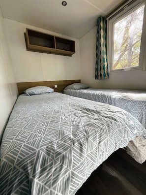 Quarto com duas camas, uma estante de madeira, janela com cortinas e uma luminária no teto.